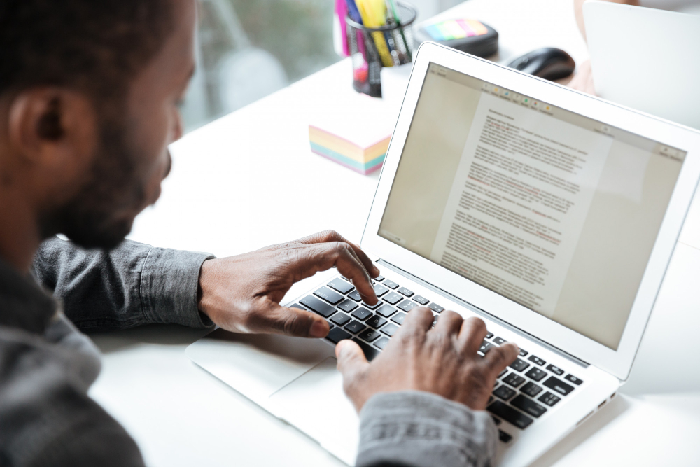 773757 - Si Quieres te lo Escribo | Hablemos de Marketing Person typing on a silver laptop with a long document visible on the screen at a bright desk.