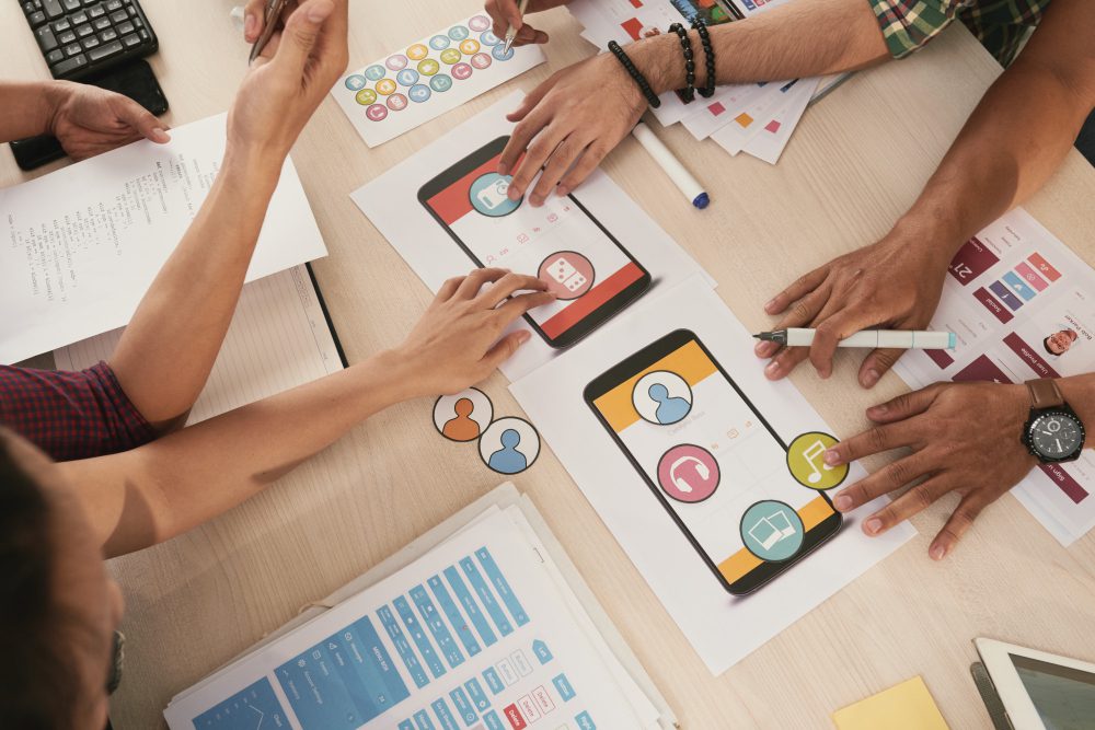 Teamwork scene with people reviewing app mockups on tablets and papers on a table
