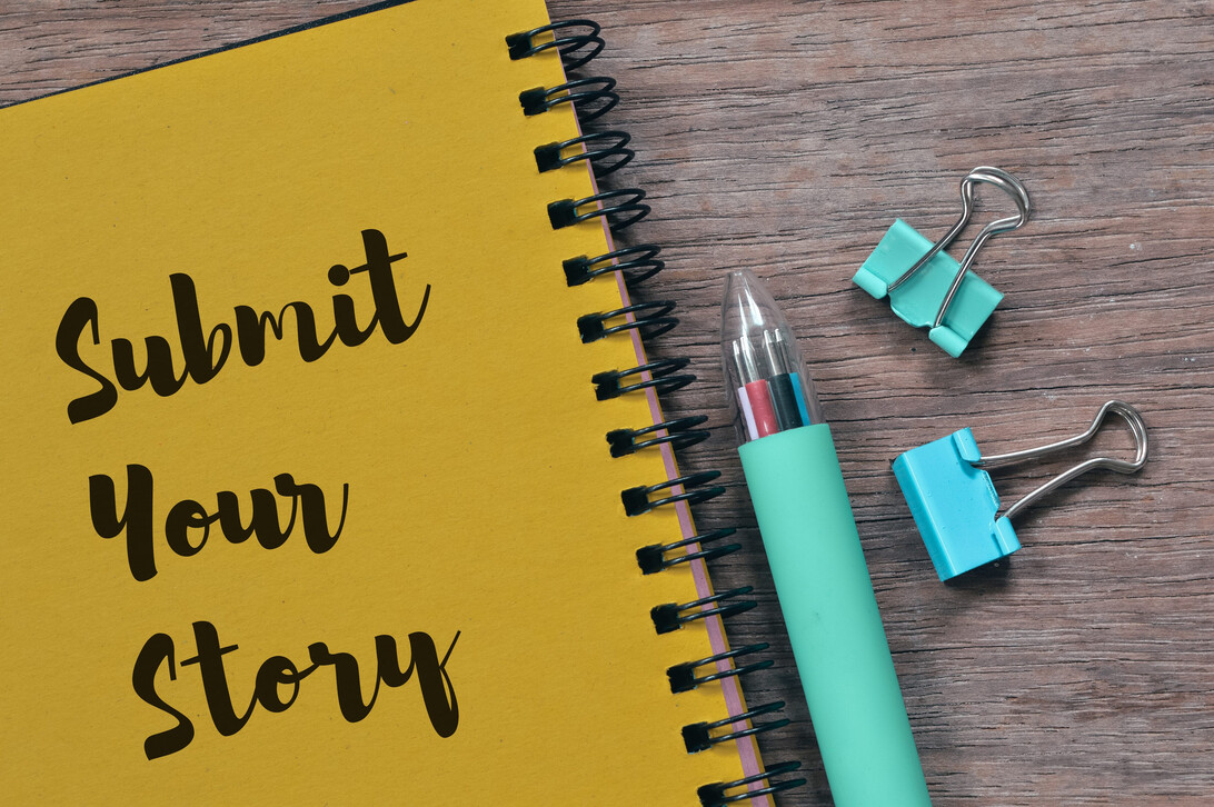 Top view of pen paper clips and notebook written with SUBMIT YOUR STORY | Hablemos de Marketing